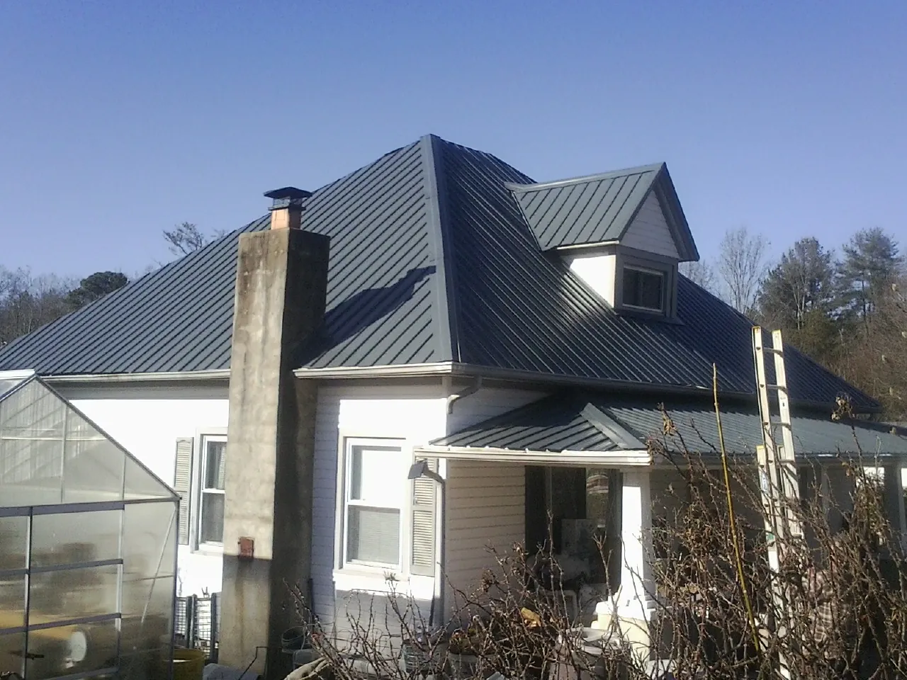 Dark blue standing seam metal roof on a white farmhouse with dormer — Slate & Tile Roof Repair by Roofing Brothers in Marston