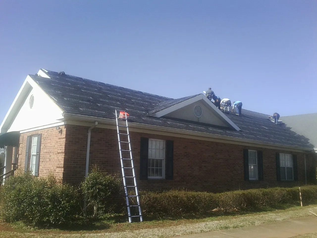 Crew tearing shingles off a brick ranch roof with a ladder set — Emergency Roof Repair work by our crew in Marston