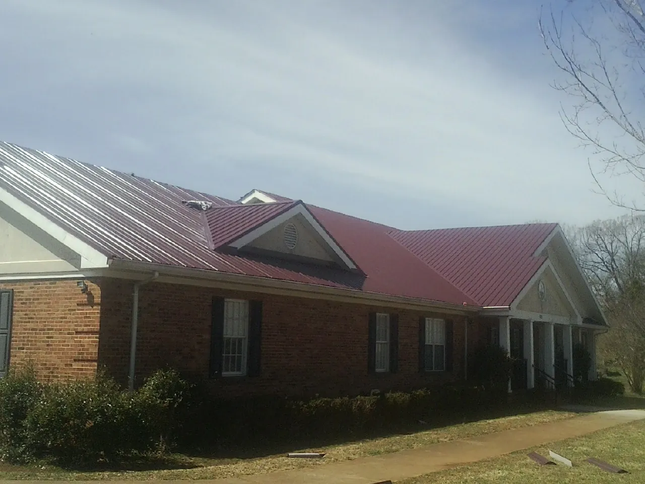 Red metal roof with gabled entries on a long brick building, from a Hail Damage Roof Repair job in Marston