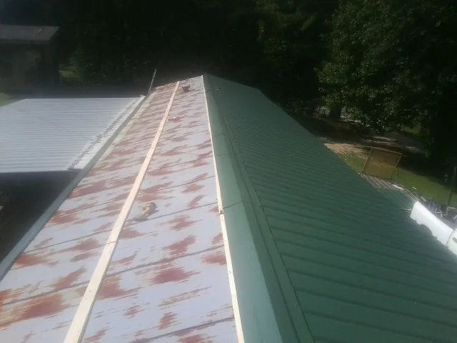 Old rusted panels beside newly installed green metal roofing — Wind Damage Roof Repair by Roofing Brothers in Marston