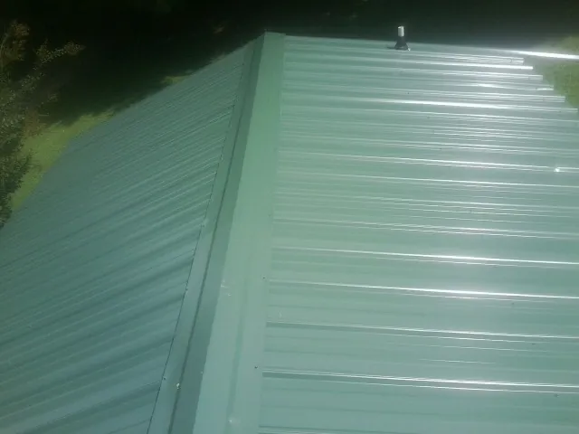 New green metal panels meeting at the ridge of a roof — Flat Roof Repair work by our crew in Marston