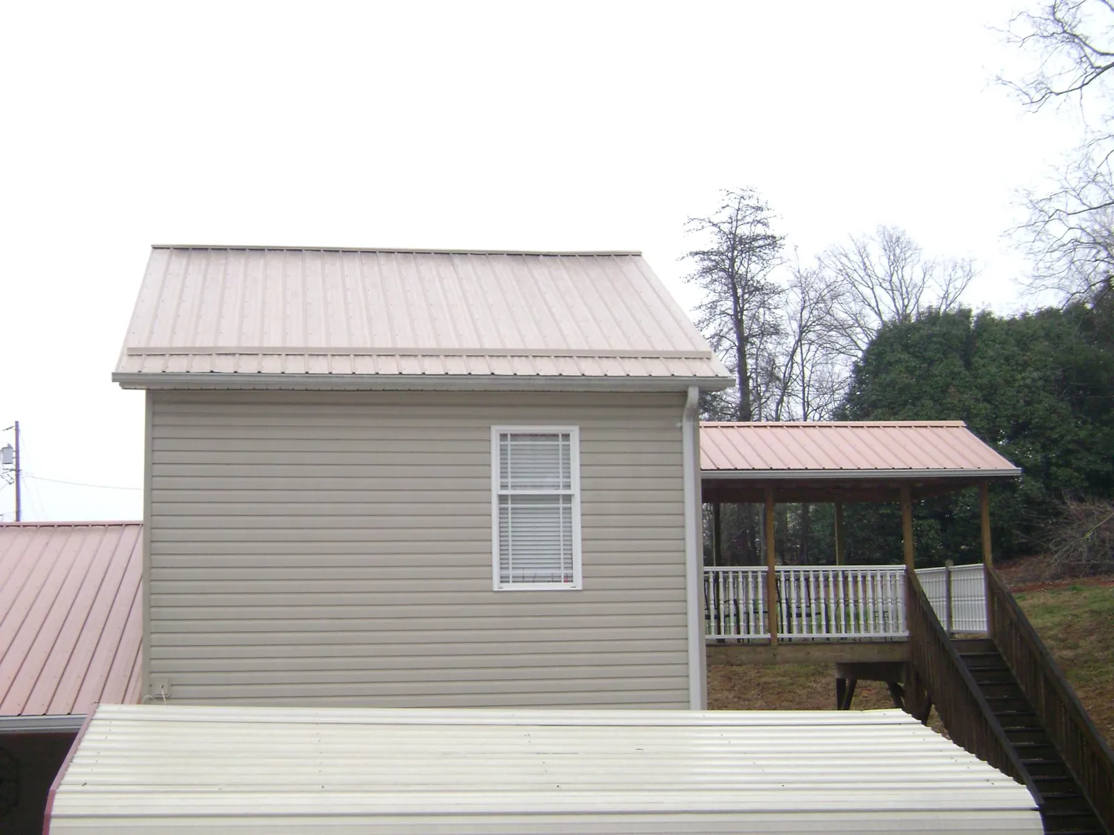 Tan metal roofs on a two story addition and attached porch, from a Roof Replacement job in Marston